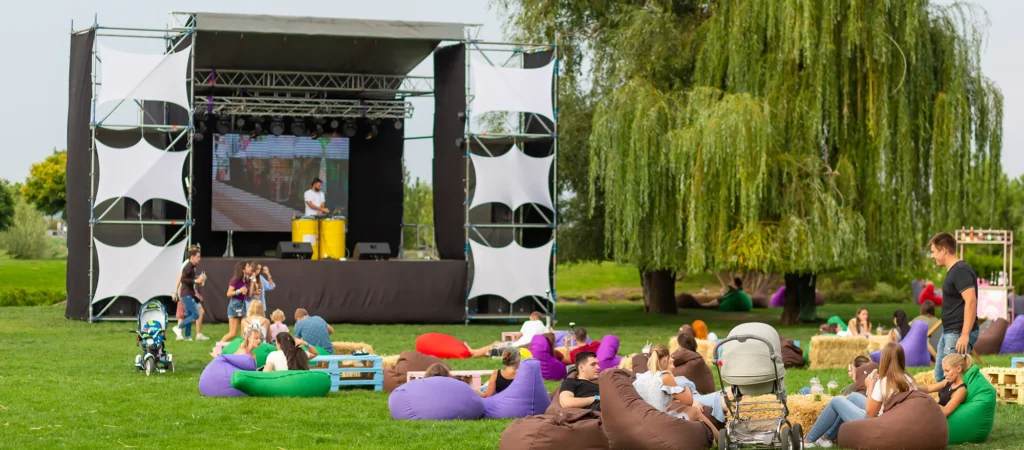 Outdoor cinema PA system, and relaxed seating on grass, showcasing a casual event setup with bean bags, hay bales, and a movie playing