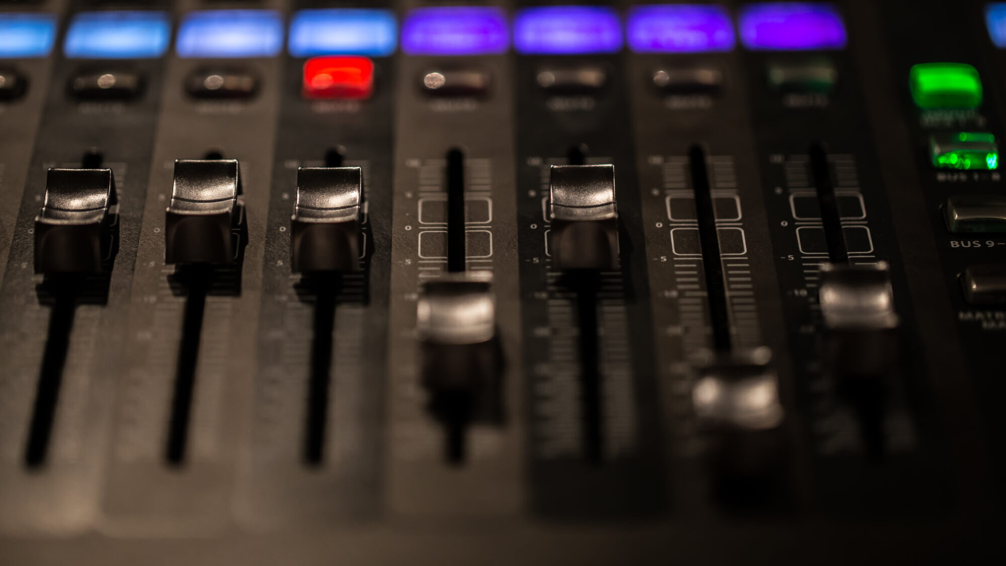 Close-up view of an audio mixing desk with sliders and lit controls, used for managing live sound at events
