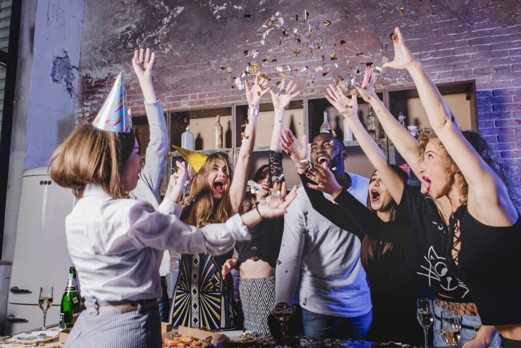Group of friends celebrating at an indoor party with confetti, drinks, and music in a lively, festive atmosphere