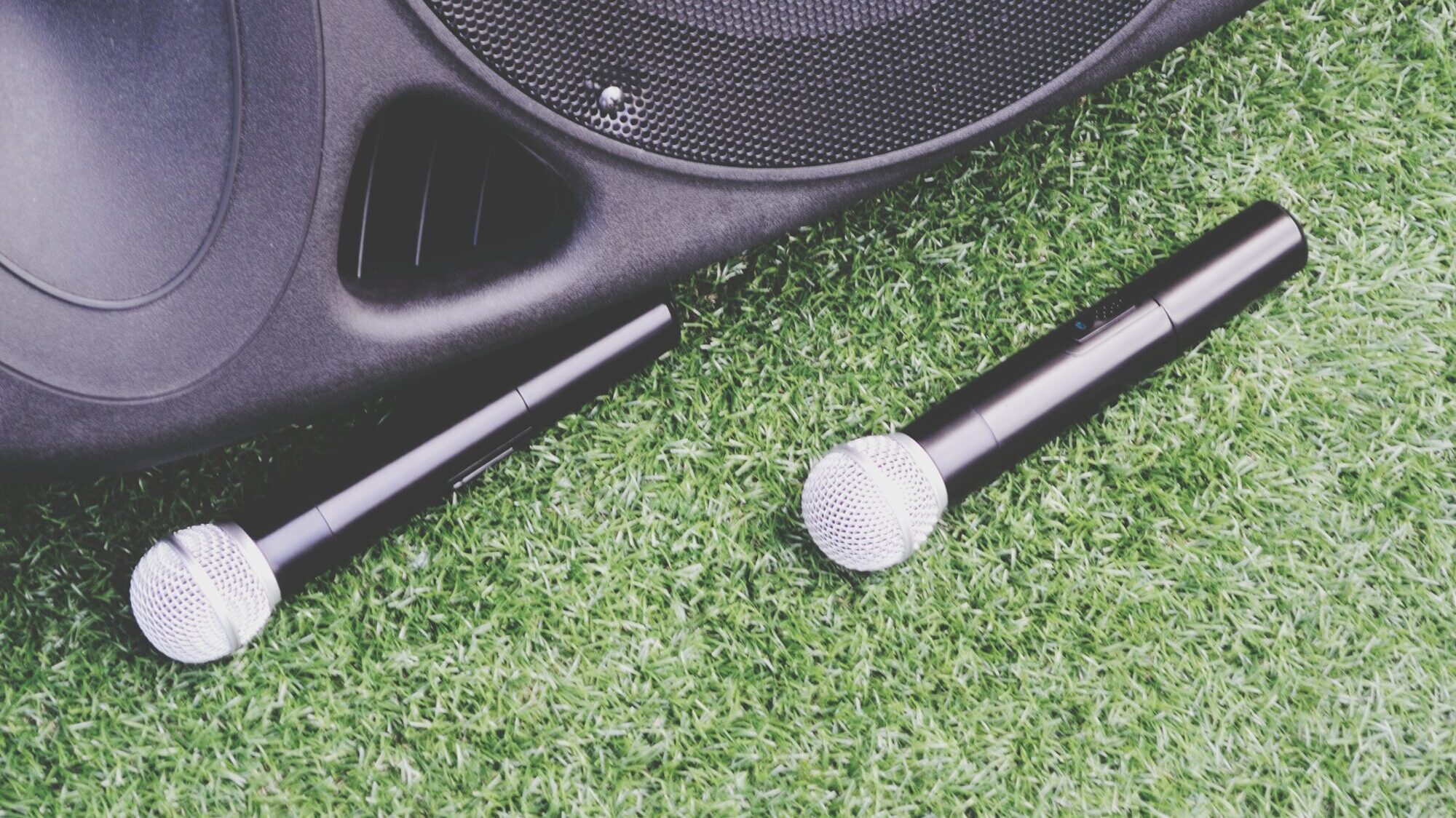 Two wireless microphones and a portable PA speaker resting on grass, ready for an outdoor event or announcement