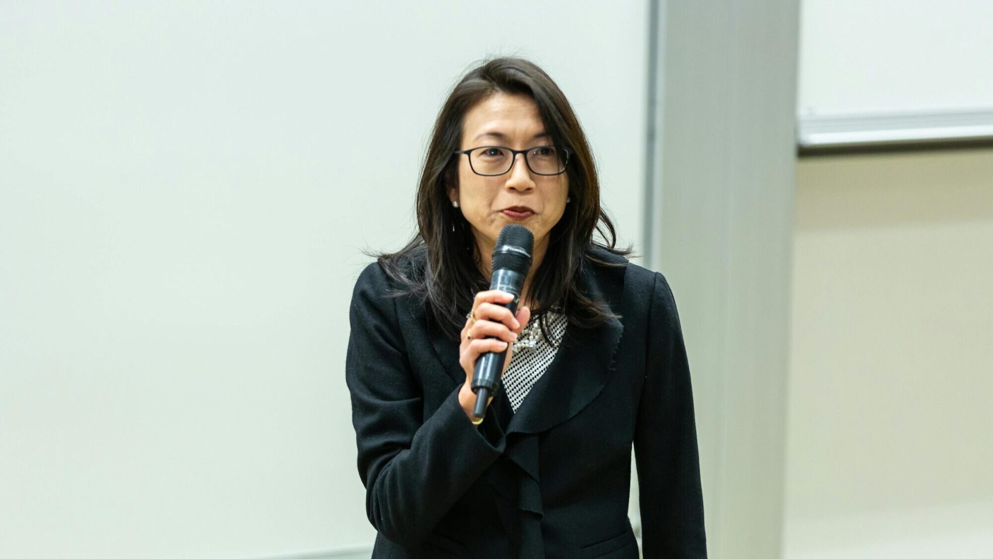 Presenter using a handheld microphone during an indoor talk, demonstrating typical use of a wired or wireless mic in a professional setting