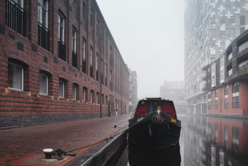 Narrowboat moored on a misty canal in Birmingham, with red-brick and modern buildings in the background.