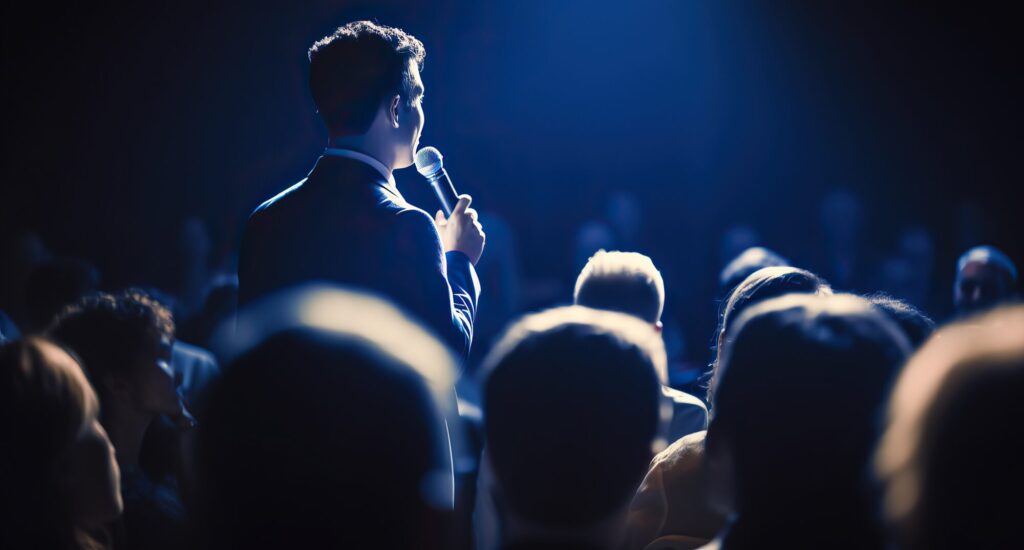 Presenter with a microphone addressing an audience at a corporate conference in Birmingham under stage lighting