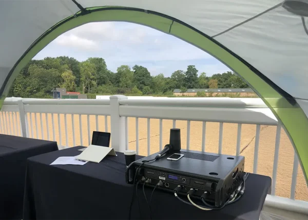 Event equipment setup under Coleman shelter with table, audio gear and microphone for outdoor use