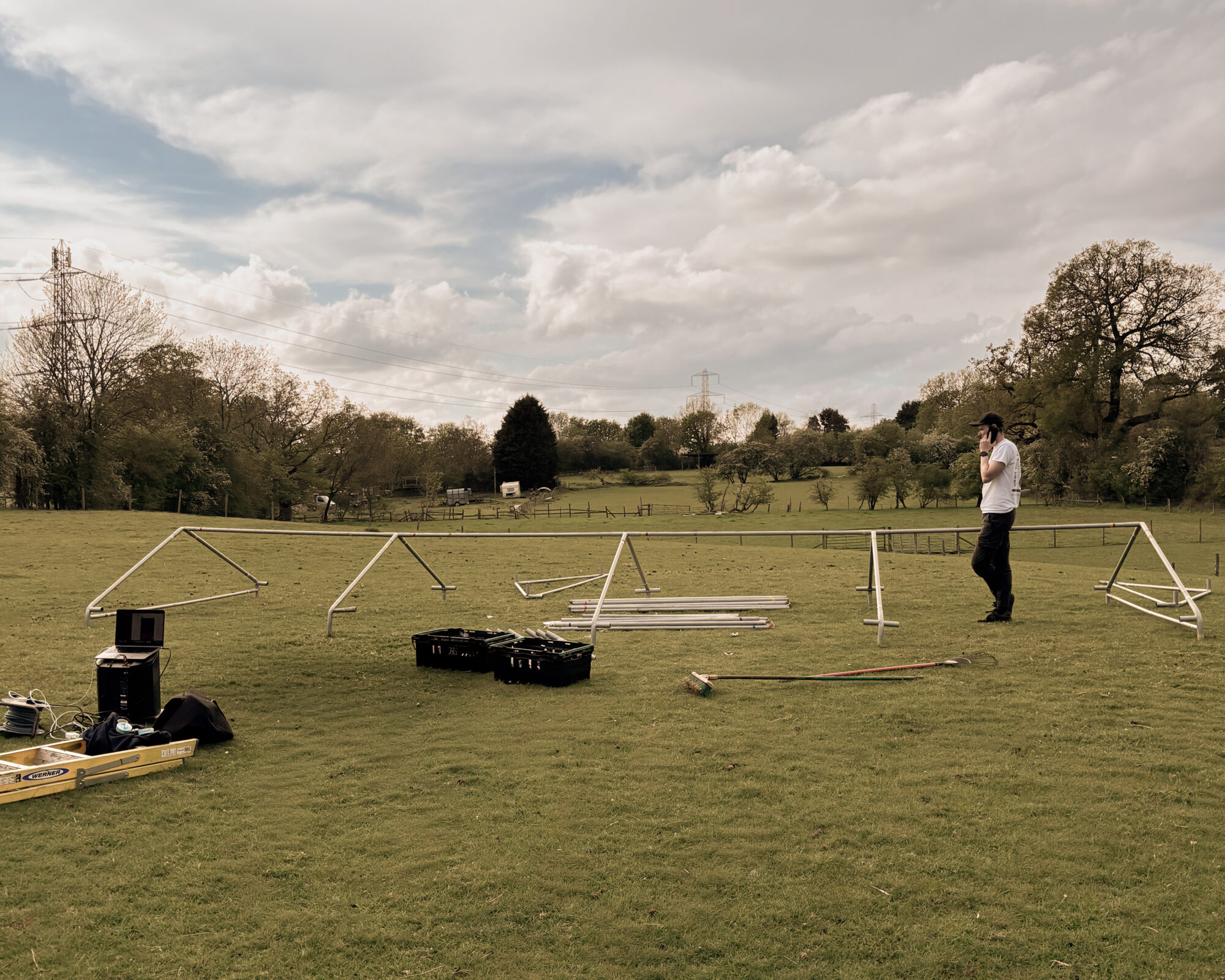 9m x 3m event tent frame being assembled on a grass field with equipment boxes and tools nearby.