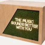 Wooden DJ booth with The Music Sounds Better With You neon sign and foliage panel