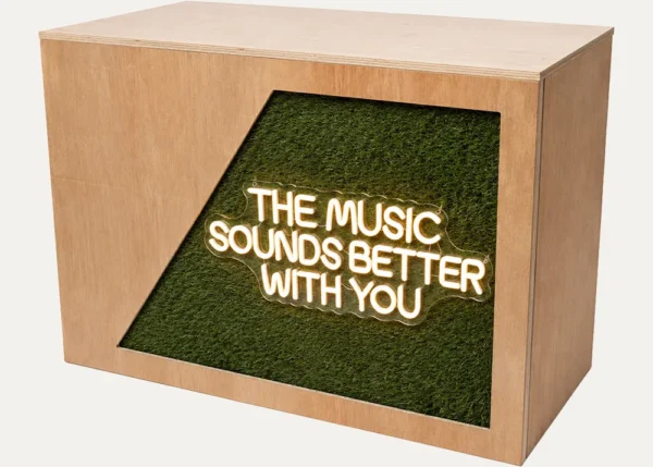Wooden DJ booth with The Music Sounds Better With You neon sign and foliage panel