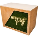 Wooden DJ booth with green foliage panel and illuminated Let’s Party sign for event hire setup