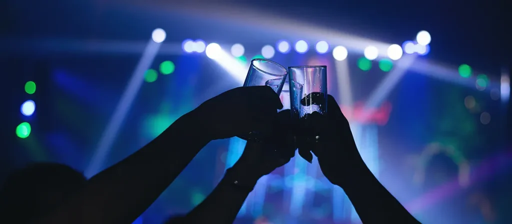 `Party guests raising glasses with colourful event lighting in the background