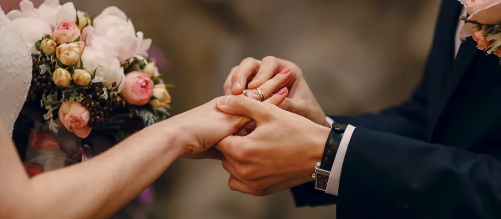Bride and groom exchanging wedding rings during a ceremony with floral bouquet in the background