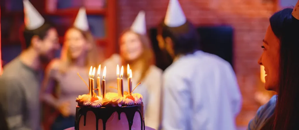 Birthday cake with lit candles at a party with guests celebrating in the background
