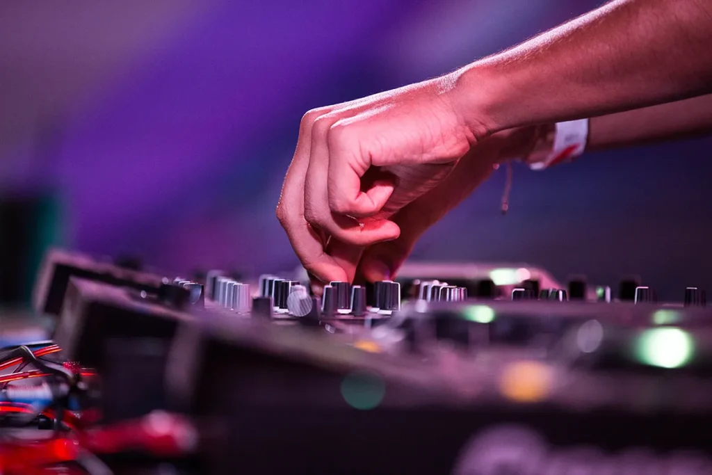DJ adjusting audio mixer controls under purple event lighting for professional DJ equipment hire