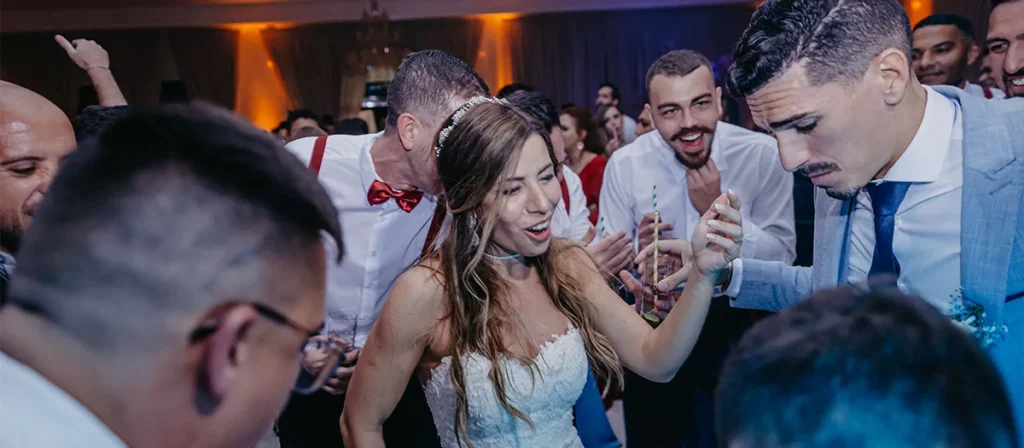 Bride and groom celebrating on a packed wedding dancefloor with guests gathered around them.